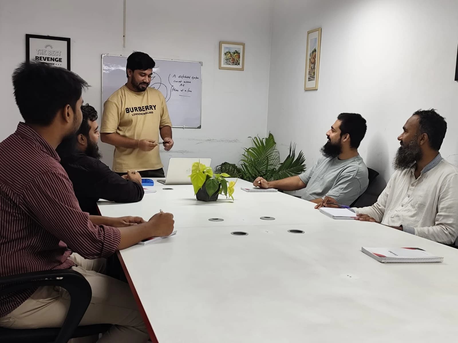 Team members around a meeting table while a colleague presents at a whiteboard